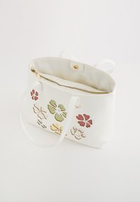 Witte leren handtas met bloemvormige uitsnijdingen in roze, groen en geel. Voorzien van een ritssluiting en twee schouderbanden. Soepele textuur.