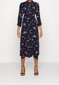 Květinové šaty s námořnickým pozadím, zdobené růžovými a zelenými květy, s knoflíkovou přední částí, tříčtvrtinovými rukávy a páskem v pase.