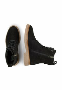 Sorte ankelstøvler i ruskind med en tekstureret brun sål, der har snørebånd og lynlåslukning. Rundt snudedesign, minimalistisk stil.