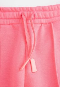 R óżowe spodnie dresowe z sznurkiem ze plastikowymi końcówkami, wykonane z miękkiego materiału, z ribbowanym pasem i widoczną teksturą.