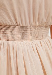 Robe texturée pêche avec une taille smockée et une jupe plissée fluide. Le tissu semble doux et léger.