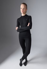 Czarna bluzka z długim rękawem i zamkiem przy kołnierzu, dopasowane czarne legginsy i ciemne skarpetki. Gładki materiał, minimalna marka, elegancki design.