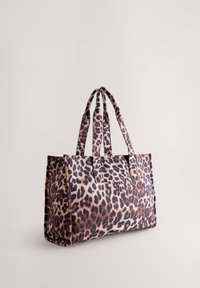 Geantă tote din material cu imprimeu leopard, cu două mânere robuste, formă rectangulară și textură netedă. Prezintă pete marron închis și deschis pe un fundal bej.