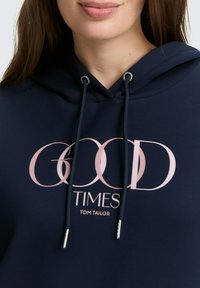Sötétkék kapucnis felső, húzózsinórral és ezüst színű fém részekkel, elöl rózsaszín grafikával "GOOD TIMES" és "TOM TAILOR" felirattal.