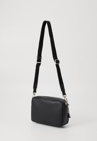 Borsa a tracolla in pelle nera testurizzata con tracolla regolabile, hardware in argento, chiusura zip, forma rettangolare e design pulito.
