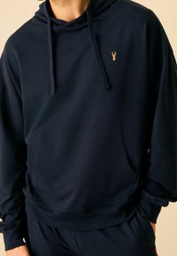 Granatowa bluza z kapturem wykonana z miękkiego materiału, posiadająca przednią kieszeń oraz haftowane logo na klatce piersiowej.