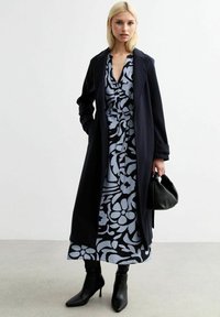 Marineblauer Mantel und hellblaues Blumenkleid mit taillierter Taille, schwarze Stilettos und eine schwarze Handtasche. Glattes Material, elegantes Design.