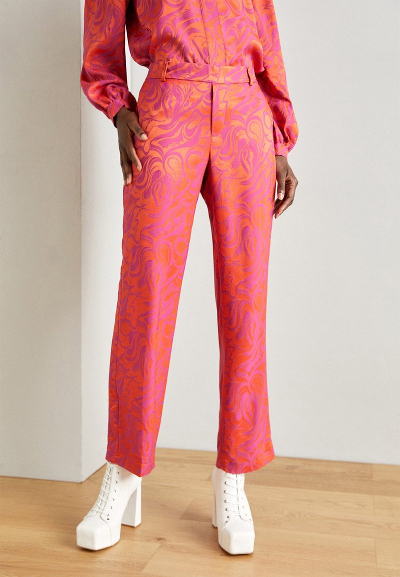 Personne portant un pantalon droit taille haute et un haut assorti à manches longues avec un motif abstrait orange et rose, ainsi que des bottes blanches à plateforme à lacets.