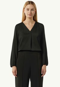 Schwarze Bluse mit V-Ausschnitt, langen Ärmeln und plissierter Vorderseite. Der Stoff hat eine glatte Textur und ein leicht glänzendes Finish.
