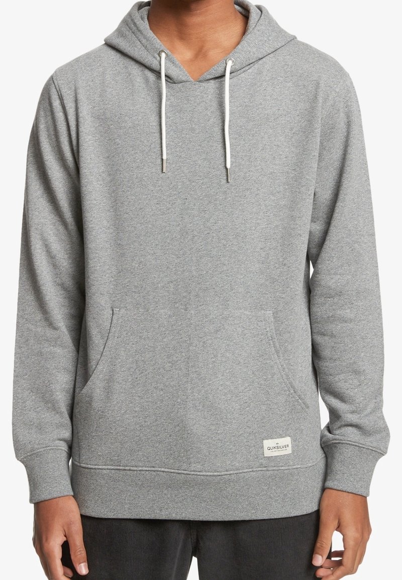 Personne portant un sweat à capuche gris clair avec des cordons blancs et une poche kangourou à l'avant.
