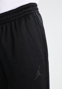 Black athletic joggers with an elastic waistband, side pockets, and a grey Jumpman logo on the thigh. Made from smooth, breathable fabric.