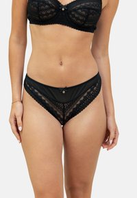 Un bralette en dentelle noire et des culottes assorties présentent des motifs géométriques et des finitions délicates. Le soutien-gorge dispose d'une armature, avec un petit nœud accentué au centre.