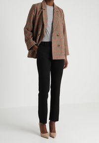 Dvojřadý kostkovaný blazer v hnědé a béžové barvě, zkombinovaný se šedým tričkem a černými skinny kalhotami; nude vysoké podpatky dokončují celkový vzhled.