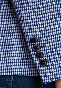 Niebieska i biała tkanina w wzór houndstooth z teksturowanym wykończeniem; posiada cztery czarne guziki na mankiecie oznaczone napisem "LANCERTO."