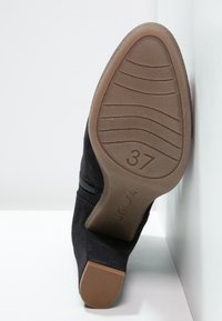 Czarne zamszowe botki za kostkę z teksturowaną brązową podeszwą, z bocznym zapięciem na zamek i wyprofilowanym obcasem. Rozmiar oznaczony jako 37 na podeszwie.