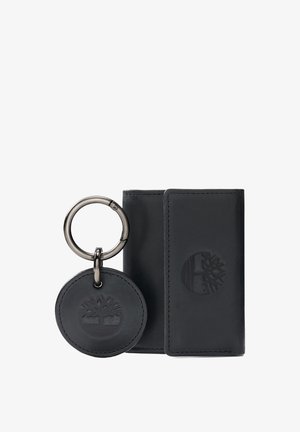Portefeuille en cuir noir avec un porte-clés circulaire. Le portefeuille présente un logo d'arbre en relief, des coutures contrastées et une forme rectangulaire élégante. Le porte-clés comprend un anneau et un design en relief assorti.