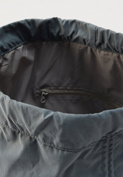 Γκρι τσάντα από νάιλον με σφηκοειδές επάνω άκρο, λεία υφή και εσωτερική τσέπη με φερμουάρ που αναδεικνύει μια διακριτική λάμψη.