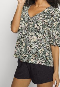 Top s květinovým potiskem na černém pozadí, zdobený pastelovými květinami, véčkovým výstřihem a nafouklými rukávy. Kombinováno s černými texturovanými šortkami.