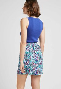 Haut sans manches bleu vif associé à une jupe à motifs floraux colorés comportant des feuilles vertes et des accents violets ; taille élastique.