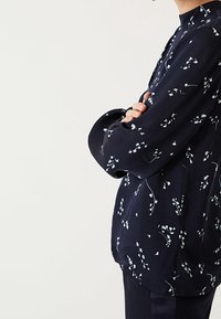 Blusa navy con stampa floreale, dotata di maniche lunghe e colletto rialzato. Realizzata in tessuto leggero con una texture liscia e una vestibilità comoda.