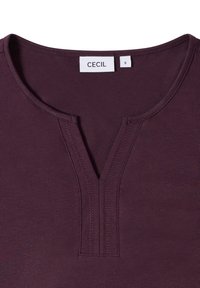 Kortärmad bordeauxfärgad topp med en rundad V-ringning, som har en knapplist och subtila sömnadsdetaljer. Etiketten läser "CECI" och storlek "S".
