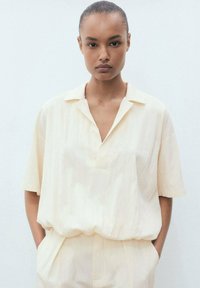 Pale yellow short-sleeve blouse with a collared neckline and a relaxed fit, made of lightweight fabric, featuring subtle vertical stripes.