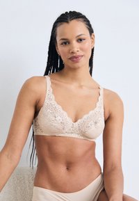 Herenkant bralette in nude kleur met geschulpte randen, verstelbare bandjes en bloemmotief. Zachte textuur met een delicate uitstraling.