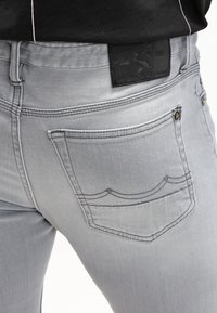 Jeans de mezclilla grises con un diseño ajustado, detalles en los bolsillos traseros y un parche de cuero en la cintura con un logotipo en relieve.