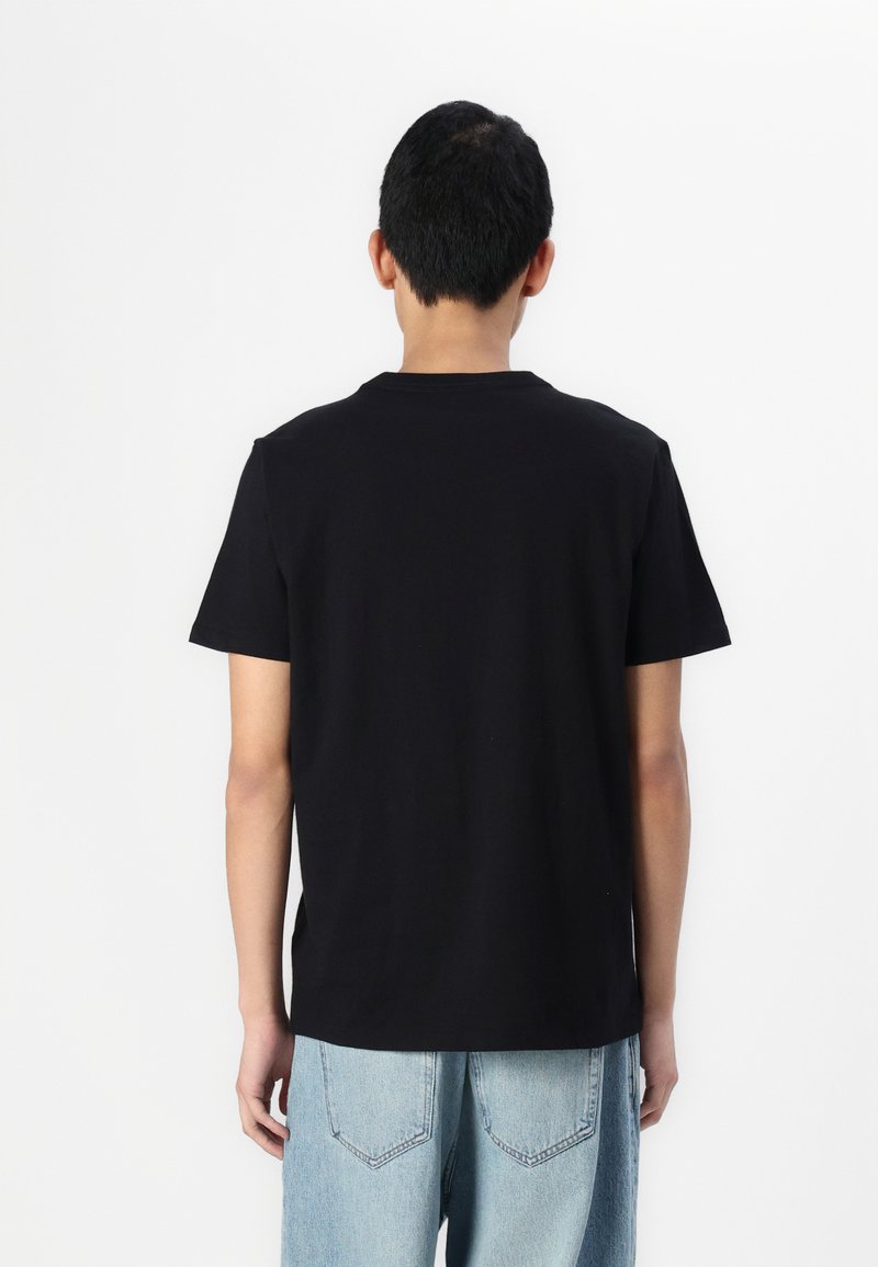 Schwarzes Baumwoll-T-Shirt mit kurzen Ärmeln und Rundhalsausschnitt, getragen mit hellblauen Jeans aus Denim, die über Rückentaschenmit Nähdetails verfügen.