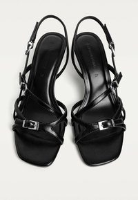 Zwarte slingback sandalen met een vierkante neus, voorzien van gekruiste banden en zilveren gespen. Gemaakt van soepel leer, hebben ze een strakke afwerking.