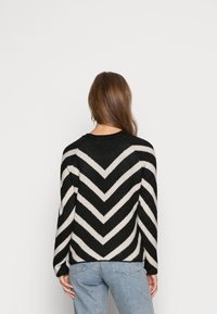 Pull en tricot doux à rayures en chevron noir et blanc, doté de manches longues et d'un col rond, associé à un jean bleu.