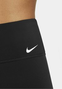 Gros plan sur la taille d'une personne portant des leggings de sport noirs taille haute avec un logo Nike blanc sur le côté gauche.
