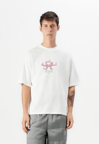 White cotton t-shirt with short sleeves featuring a pink graphic design and green text "FLEX YOUR BODY, REACH YOUR MATCHA." Loose fit.