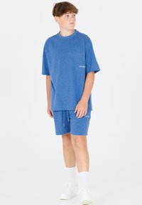 Sininen puuvillainen T-paita, jossa on lyhyet hihat ja pyöreä pääntie, yhdistetty vastaaviin shortseihin. Molemmissa osissa on hienovarainen logo ja nyöritys.