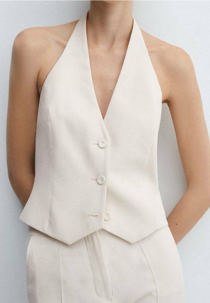 Gilet sans manches crème col halter avec trois boutons, porté avec un pantalon taille haute assorti, sur un fond clair uni.