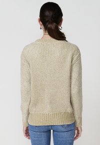 Beige kootud kampsun tekstuurse mustriga, ribaga äärega ja mansetiga. Seljal on lõdva lõikega ja ümara kaelusega, sobib siniste teksadega.