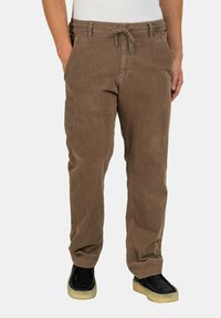 Brown corduroy pants with an elastic waistband and drawstring. Features side pockets and a relaxed fit. Paired with black shoes.