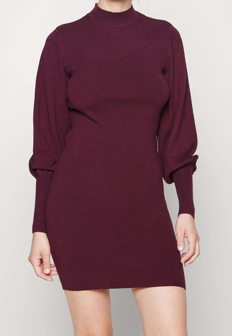 Abito a maglia a coste in Borgogna, con collo alto, vestibilità aderente e maniche lunghe a sbuffo. Il tessuto ha una texture liscia con polsini elastici.