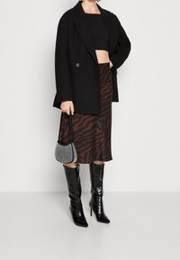 Sort dobbelt-brystet blazer over en tætsiddende sort crop top, kombineret med en brun zebra-mønstret midi-skjorte, knæhøje, skinnende sorte støvler og en lille sølv taske.