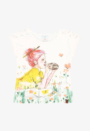 Fille aux cheveux roses en chemise jaune tient un appareil photo allongée dans l'herbe avec des fleurs, des papillons et un carnet de croquis ouvert avec une palette de peinture.