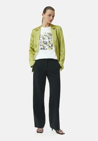 Groene satijnen blazer over een witte graphic t-shirt met bloemdesign, zwarte wijde broek en zwarte sandaaltjes met bandjes. Zachte texturen en een getailleerde pasvorm.