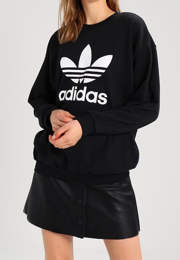 Svart sweatshirt med en vit Adidas-logotyp, med rund halsringning och ribbade ärmslut. Kombinerad med en svart läder minikjol.