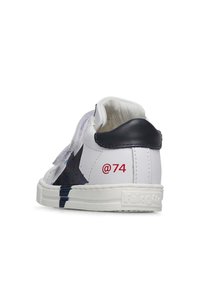 Sneaker bianca con design a stella blu navy, dettagli perforati e particolare rosso "@74". Presenta un tallone nero testurizzato e suola bianca. Cinghia in velcro.