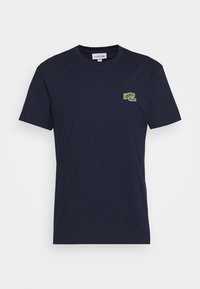 Marinblå bomullströja med rund hals och korta ärmar. Har en liten grön Lacoste-logotyp broderad på vänster bröst.