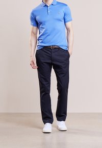 Polo shirt azzurro abbinato a pantaloni blu scuro e sneakers bianche. La maglietta presenta un colletto e un piccolo logo sul petto.