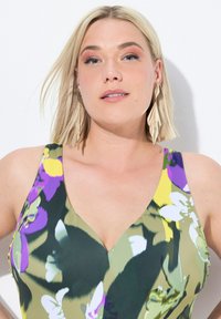 Plavky s květinovým potiskem, které mají hluboký V-výstřih, v odstínech zelené, fialové a žluté. Modelka nosí náušnice ve tvaru listů.