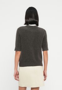 Μπλούζα με κοντά μανίκια σε σκούρο γκρι χρώμα, κατασκευασμένη από απαλό υλικό με στρογγυλή λαιμόκοψη και εφαρμοστή σχεδίαση, σε συνδυασμό με μια ανοιχτόχρωμη φούστα.