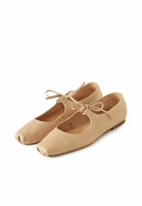 Bailarinas de cuero beige con puntas redondas, laterales cortados y detalles de lazo en la parte delantera. Suela plana con una textura suave.