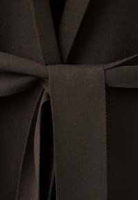 Ceinture en tissu brun foncé nouée autour d’un vêtement épais et texturé, probablement un manteau ou un peignoir.