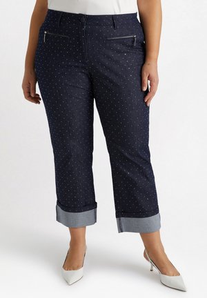 Pantaloni in denim scuro con pois bianchi, tagliati corti con orlo ripiegato e tasche frontali con zip. Vita piatta e texture liscia.